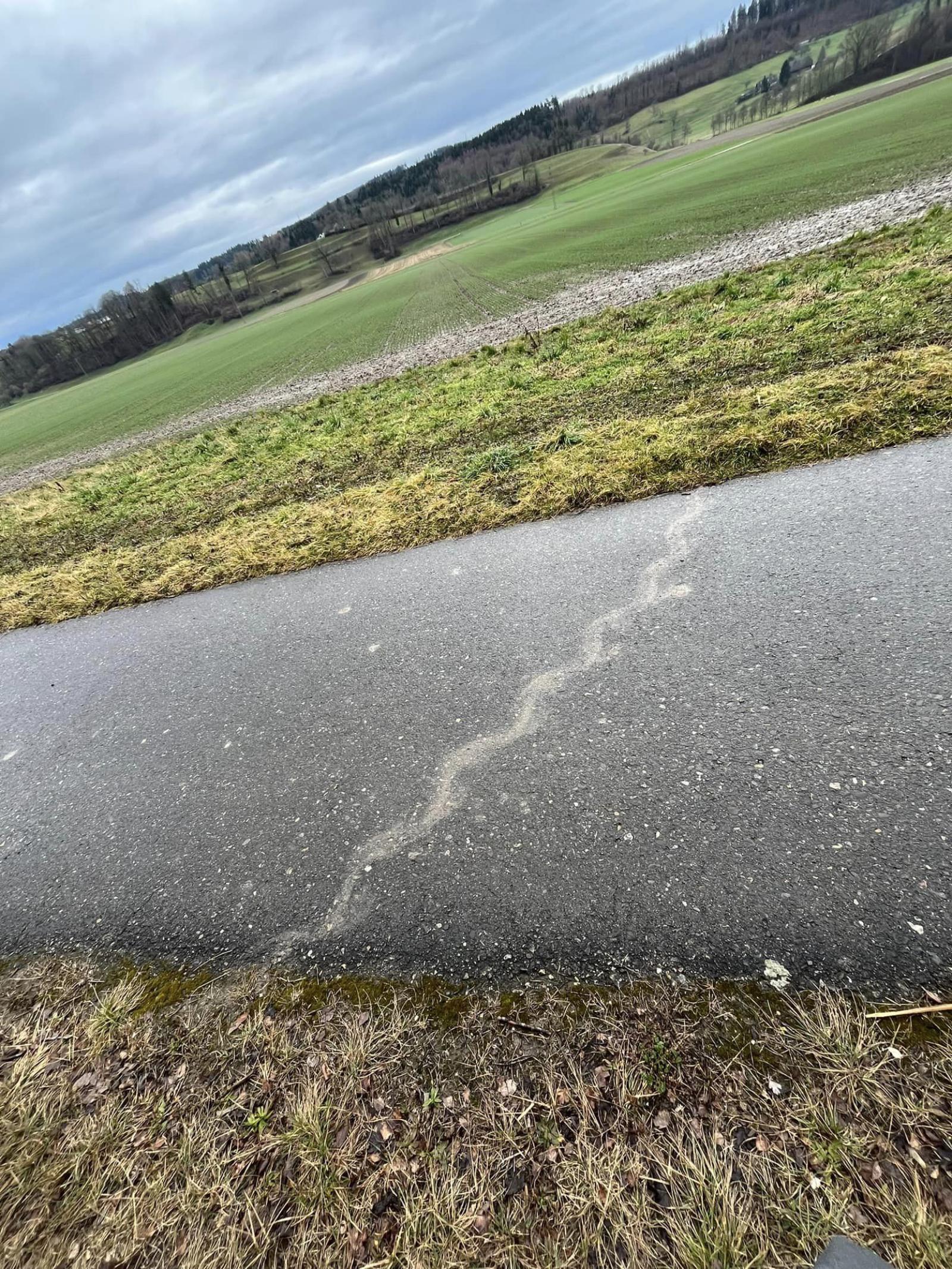 Schlammspur über Asphaltstrasse neben Landwirtschaftsland